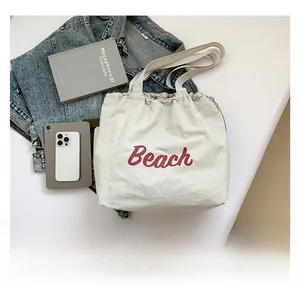 Close-up of lightweight white nylon tote bag with red Beach typography and drawstring detail