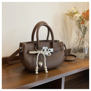 Close-up of brown lychee pattern leather bucket bag with pearl bow and heart pendant