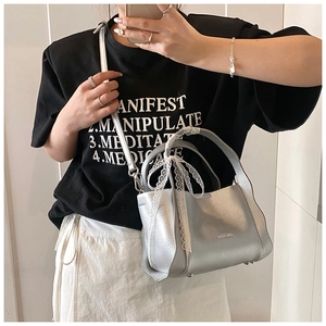 Detail of silver lychee grain leather bucket bag with a white lace bow on the handle