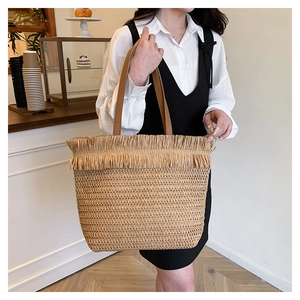 Straw tote bag detail with raffia fringe trim and brown leather handle in a cafe