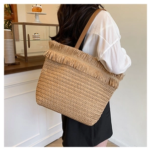 Detail of straw woven tote bag featuring long bohemian tassels and brown leather straps