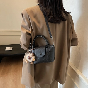 Détail d'un sac à main en cuir noir mat avec breloque lion en peluche et logo embossé
