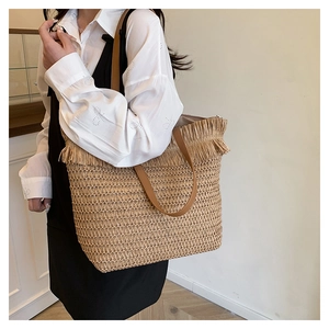Detail of straw tote bag showing dense fringe trim and brown leather shoulder straps