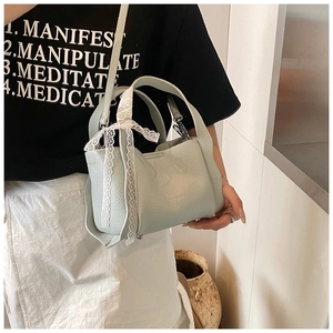 Detail of light green pebble leather bucket bag featuring a white lace bow ornament