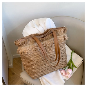 Detail of woven straw tote bag featuring decorative fringe trim and a zipper closure