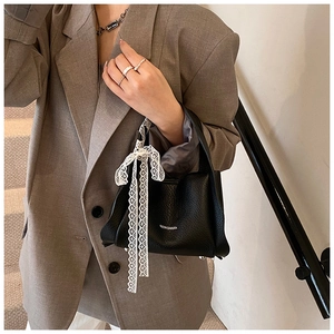 Detail of black lychee leather bucket bag with a delicate white lace bow and metal feet
