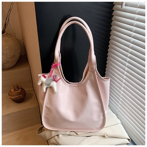 Pink tote bag detail with white pony pendant and embossed logo in soft natural light