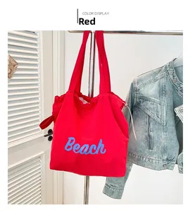 Detail of red canvas tote bag with blue Beach lettering and matching shoulder strap