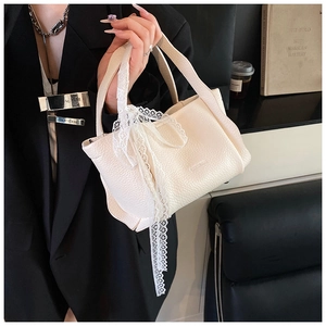 Detail of cream bucket bag with lychee texture leather and elegant white lace ribbon bow