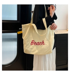Detail of a cream canvas tote bag with red Beach text on a shoulder strap model
