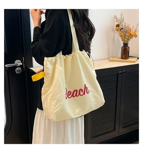 Detail of beige tote bag featuring red Beach print and bright yellow shoulder strap