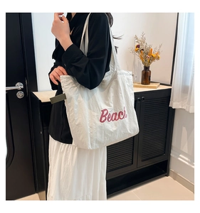 Close-up of a white pleated tote bag featuring red Beach text and olive green strap detail