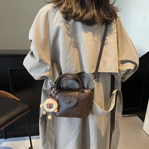 Sac à main vintage marron foncé avec charme en peluche porté sur un trench-coat beige