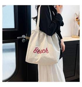 Detail of off-white tote bag with red Beach text and secure drawstring closure