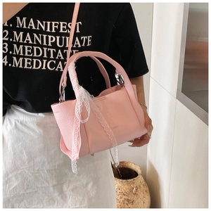 Detail showing the pink litchi grain texture and elegant white lace on the handbag