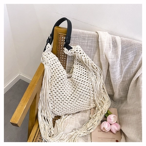 Close-up of beige crochet tote bag with long fringe details and black leather strap