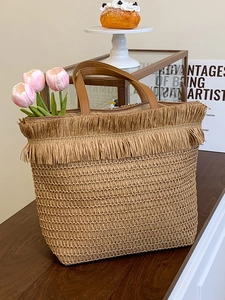 Handwoven straw tote bag with fringe detail and brown leather straps for beach holidays