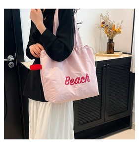Detail of light pink tote bag with red Beach letter print shown in a lifestyle setting