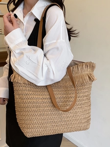 Large straw tote bag with fringe details and brown leather straps for beach holidays