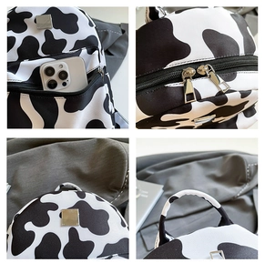 Detail of a black and white cow print canvas backpack featuring front zip pocket and top handle