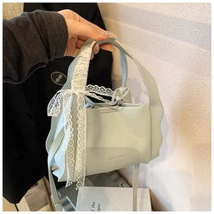 Detail view of mint green bucket bag with lychee grain leather and white lace bow