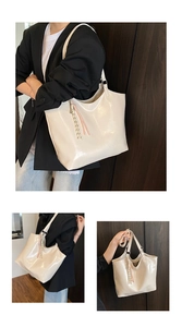 Detail of HUANKOU cream glossy tote bag with embossed logo and woven fringe tassel charm