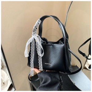 Close-up of black lychee grain leather bucket bag with white lace bow detail