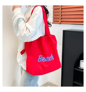 Detail shot of a red canvas tote bag with blue Beach lettering worn on the shoulder