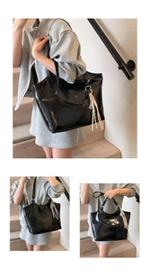 Detail of black glossy tote bag featuring embossed logo and a decorative tassel pendant