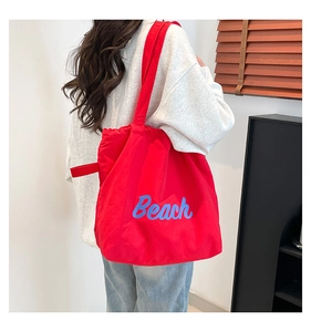 Close-up of red nylon tote bag with blue Beach text and adjustable side drawstrings