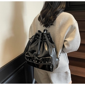 Detail of black glossy drawstring backpack featuring silver metal studs and chain straps