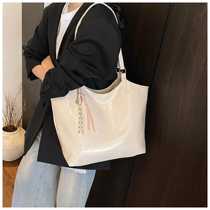 Detail of a creamy white tote bag with embossed logo and decorative tassel ornament