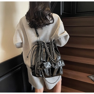 Detail of black leather bucket bag with silver chains and rivets on a model