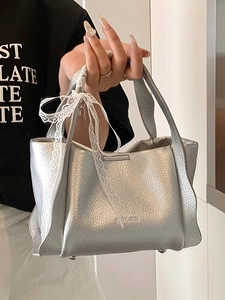 Chic silver bucket bag in lychee leather featuring a delicate lace bow and top handle