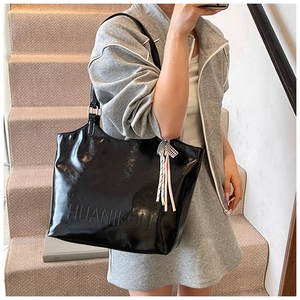 Detailed view of black oil wax leather tote bag with embossed letters and metal charms