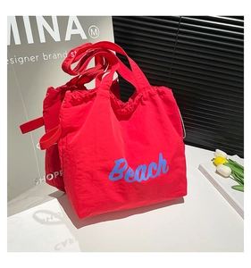 Detail of red nylon tote bag with blue Beach text and drawstring closure