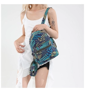 Detail of tropical leaf print on navy blue canvas backpack worn by model on white background