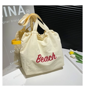 Detail of cream canvas tote bag featuring red Beach print and yellow side strap