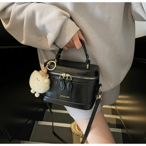 Detail of black leather box bag with gold zipper and white plush sheep charm