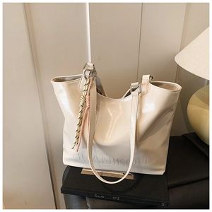 Detail of creamy white leather tote bag with braided knot charm and embossed logo