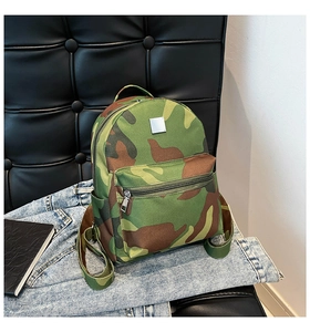Green jungle camouflage backpack with front pocket placed on denim jeans and leather background