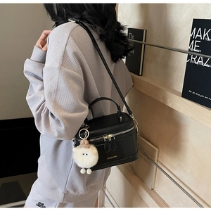 Detail of black glossy leather box bag with gold zippers and white plush sheep charm