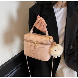 Detailed side view of beige box bag with plush monster charm and leather shoulder strap
