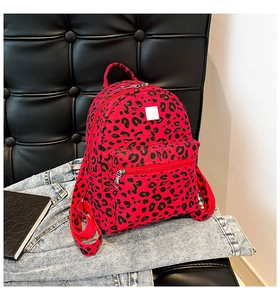 Detail of red leopard print mini backpack on black sofa with denim jacket accessory