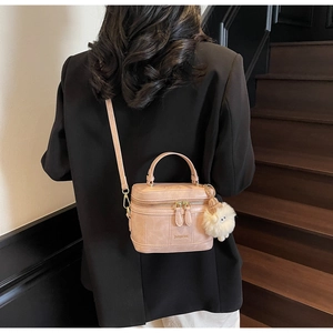 Detail of light pink vanity box bag with golden zippers and a white plush ball charm