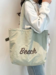Large pale green canvas tote bag with brown Beach lettering worn over the shoulder