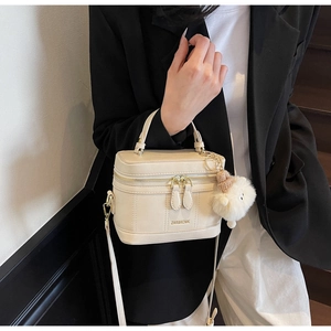 Chic beige box-style vanity bag with plush ball charm and fine shoulder strap detail