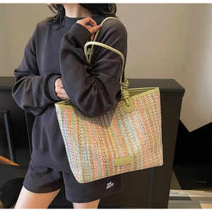 Detailed view of colorful straw woven tote bag with green leather handles and knot details