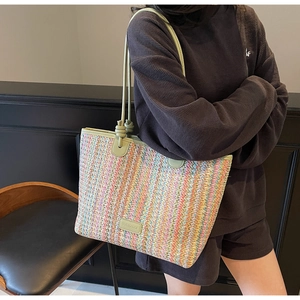 Detail of colorful striped straw tote bag with green leather shoulder strap worn by model