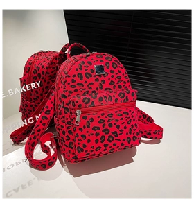 Detailed close-up of a red leopard print backpack with metal plate and silver zippers